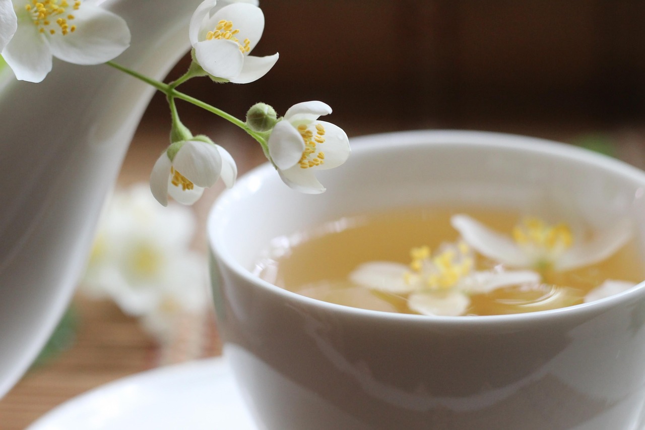 Xícara de chá com infusão de ervas e flores de jasmim ao lado de um bule.