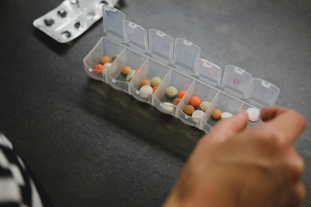 Pessoa organizando comprimidos e suplementos em um porta-comprimidos semanal sobre uma mesa.