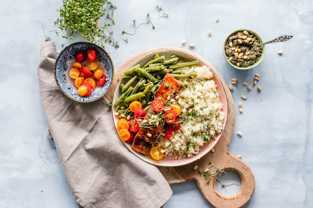 Prato saudável com salmão grelhado, cuscuz, vegetais e tomates em uma bancada de cozinha.