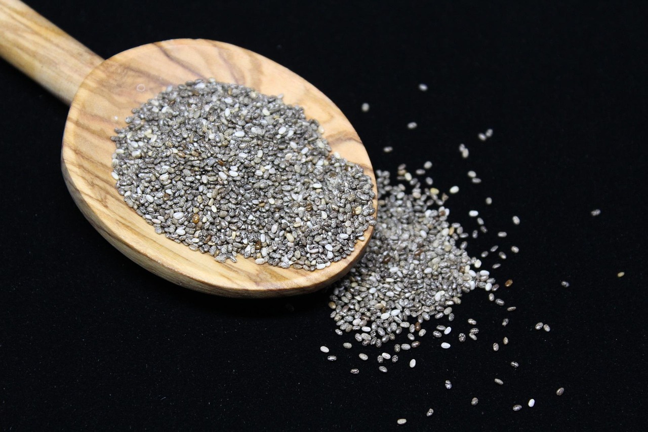 Colher de pau com sementes de chia sobre fundo preto