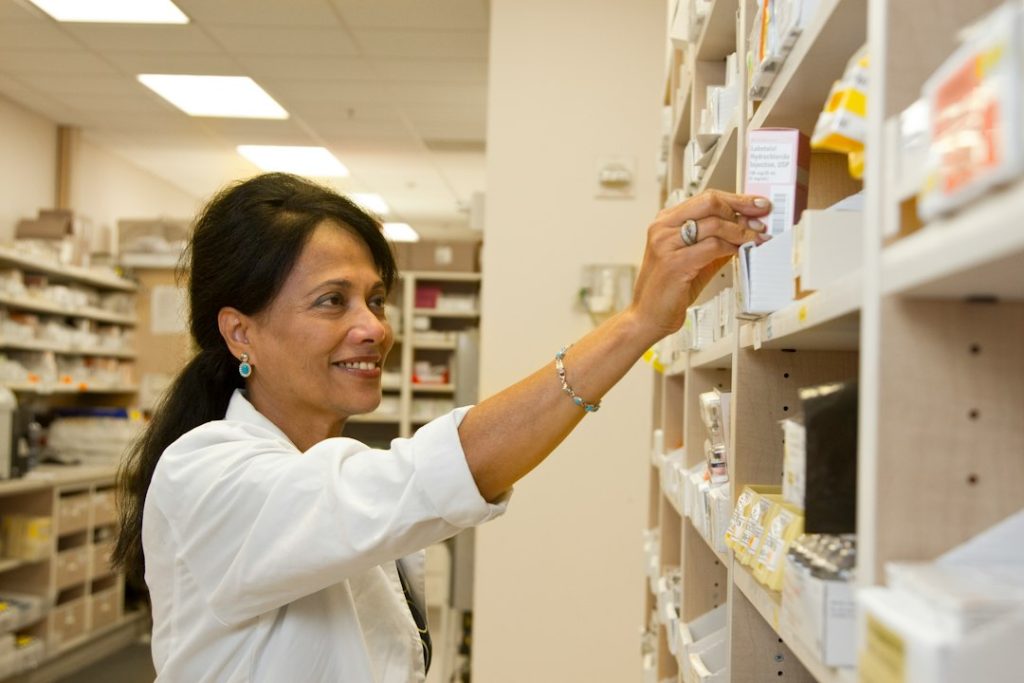 Farmacêutica organizando medicamentos e insumos na prateleira de uma farmácia