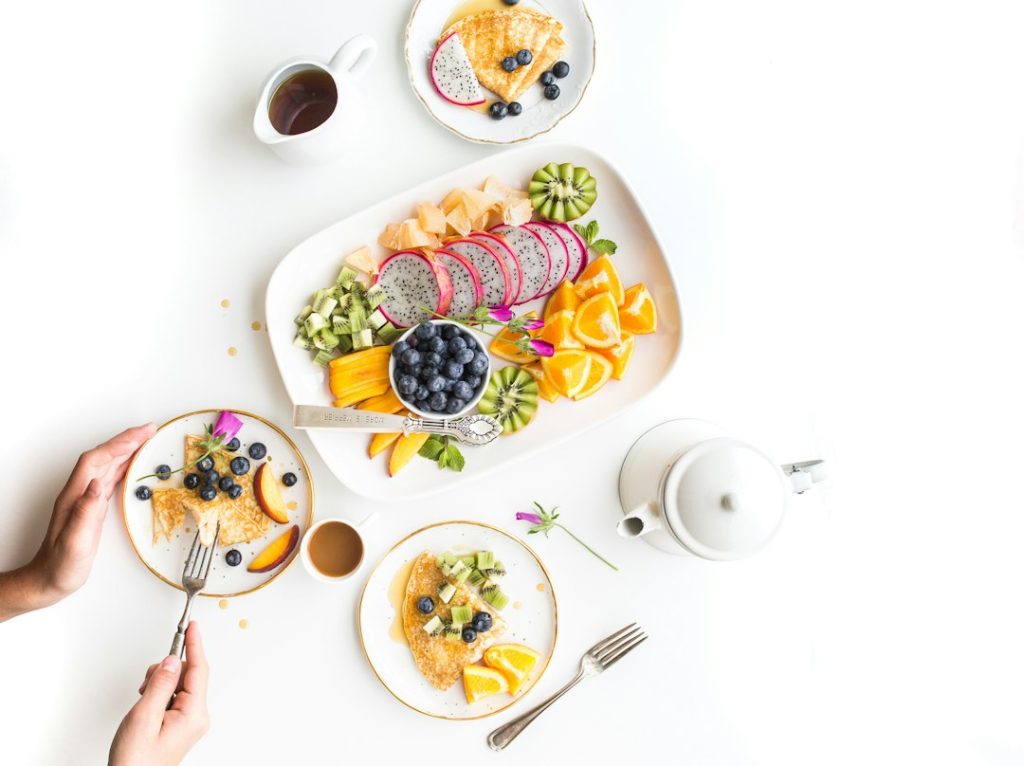 Mesa de café da manhã com panquecas, mirtilos e frutas frescas como pitaya e kiwi.
