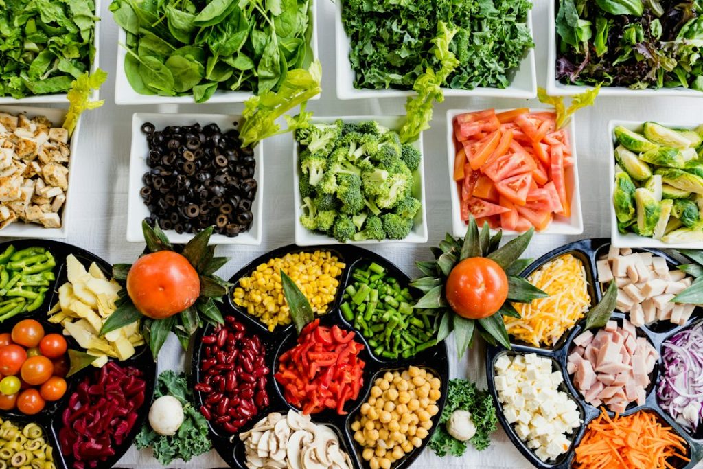 Variedade de vegetais frescos, grãos e saladas dispostos em recipientes sobre uma mesa.