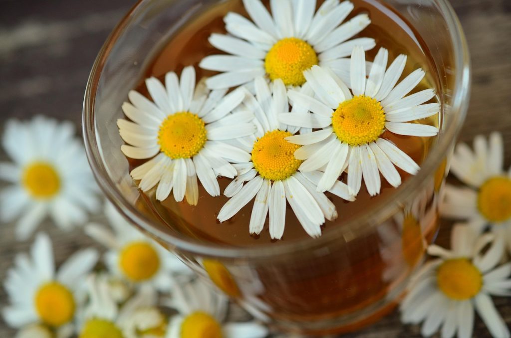 Xícara de chá com infusão de camomila e flores flutuando sobre uma mesa de madeira.