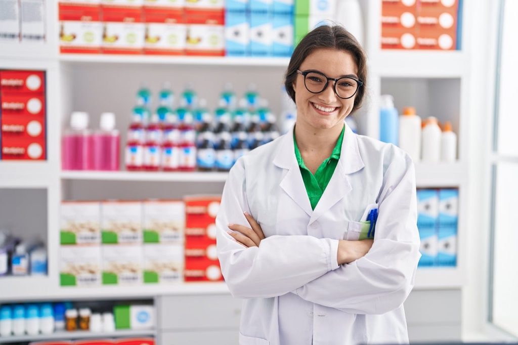Farmacêutica de jaleco e óculos sorridente em farmácia de manipulação.