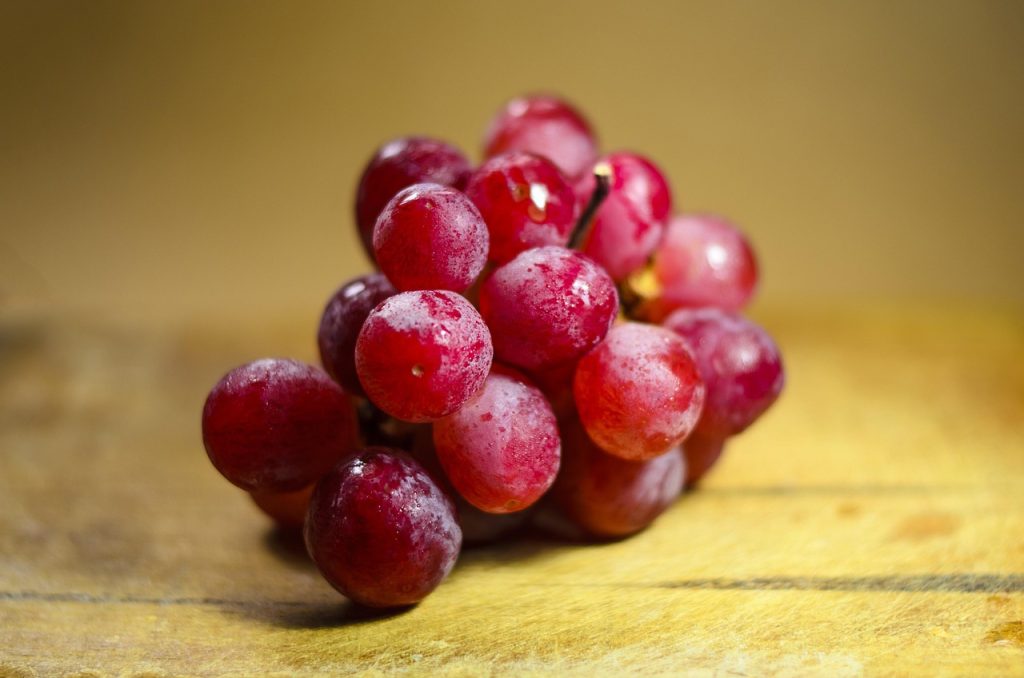 Cacho de uvas vermelhas frescas sobre superfície de madeira, principal fonte natural de resveratrol.