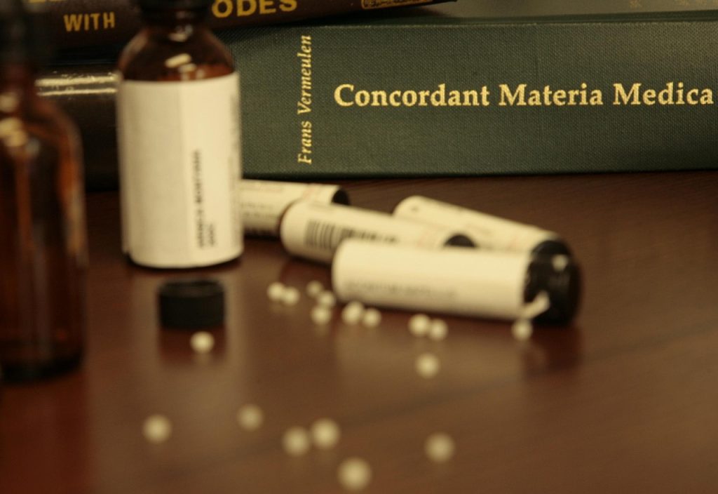 Frascos de vidro e tubos com glóbulos homeopáticos sobre uma mesa de madeira.