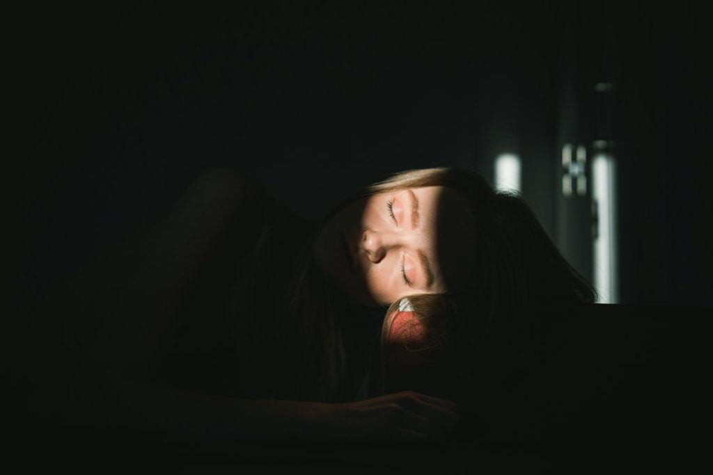 Mulher dormindo tranquilamente com o rosto iluminado suavemente em um quarto escuro.