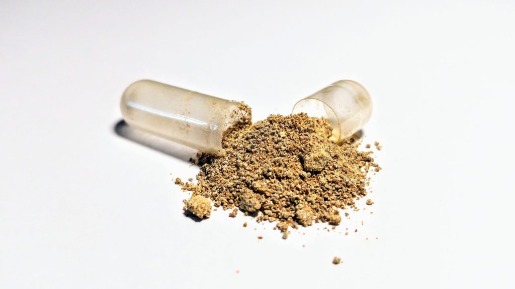 Cápsula de suplemento fitoterápico aberta com pó de ashwagandha derramado em superfície branca