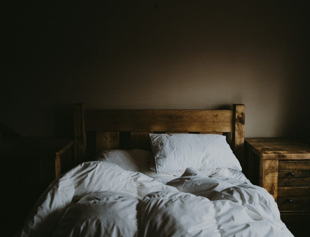 Quarto com cama de madeira, lençóis brancos e iluminação suave.