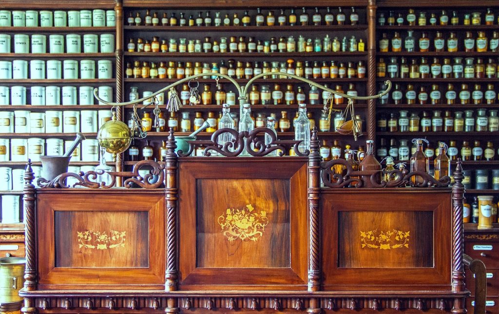 Balcão de farmácia de manipulação antigo com balança, pilão e prateleiras cheias de frascos de fórmulas.