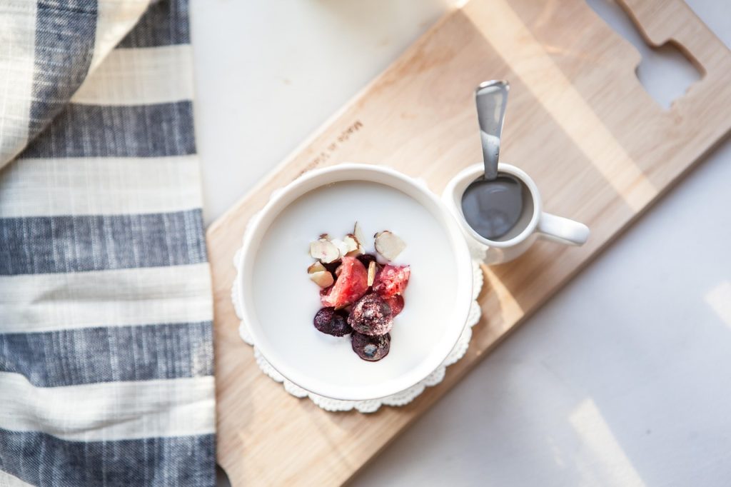 Tigela de iogurte com frutas vermelhas e amêndoas sobre tábua de madeira