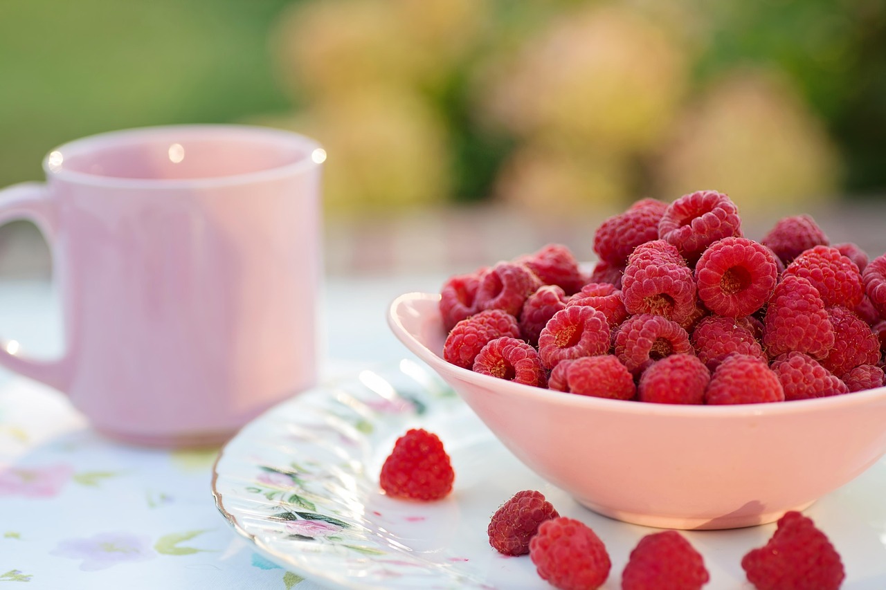 Tigela rosa com framboesas frescas sobre prato decorado e caneca ao lado