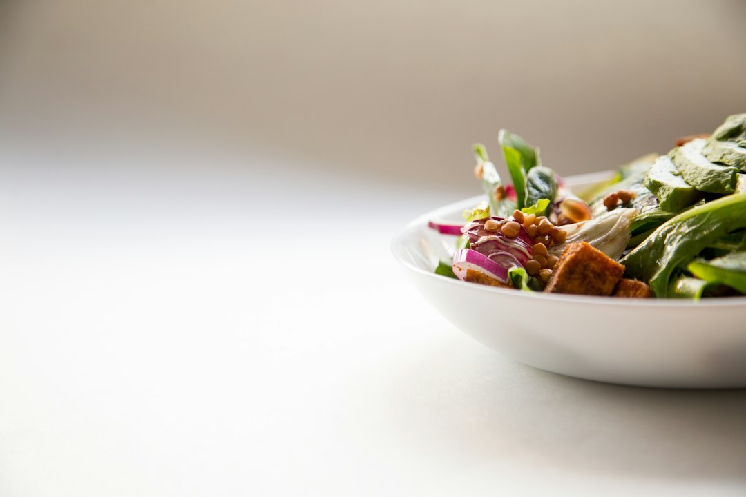 Salada fresca com folhas verdes, abacate e croutons em prato branco sobre mesa clara.
