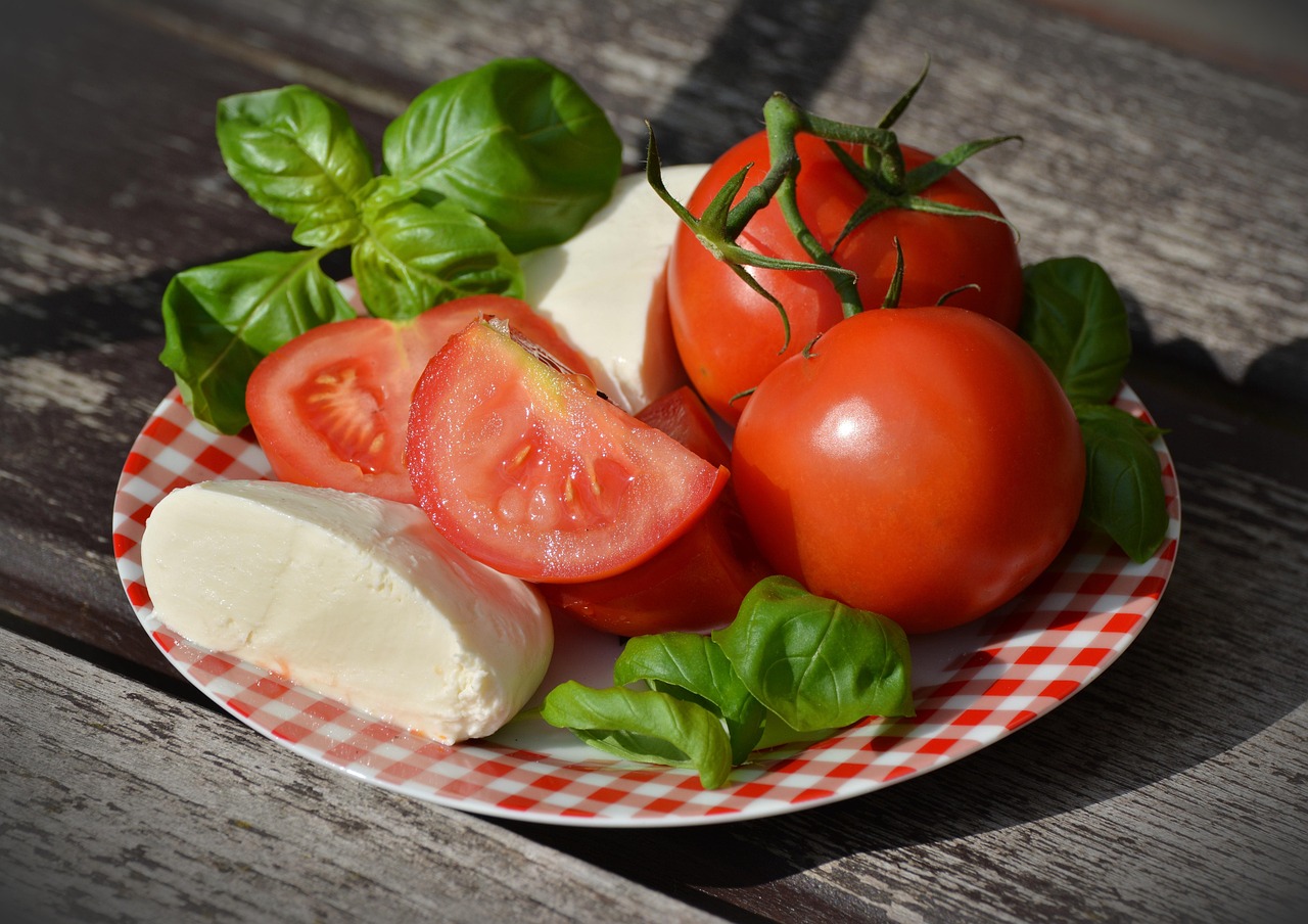 Prato com tomates fatiados, mozarela de búfala e folhas de manjericão fresco.