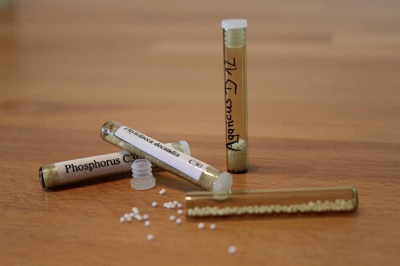 Frascos de vidro com glóbulos homeopáticos e pequenas bolinhas espalhadas sobre uma bancada de madeira.