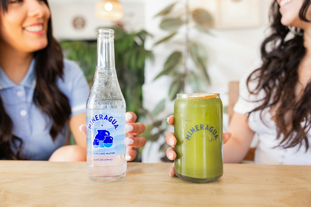 Duas mulheres sentadas à mesa com garrafa de água mineral e copo com bebida verde e limão.