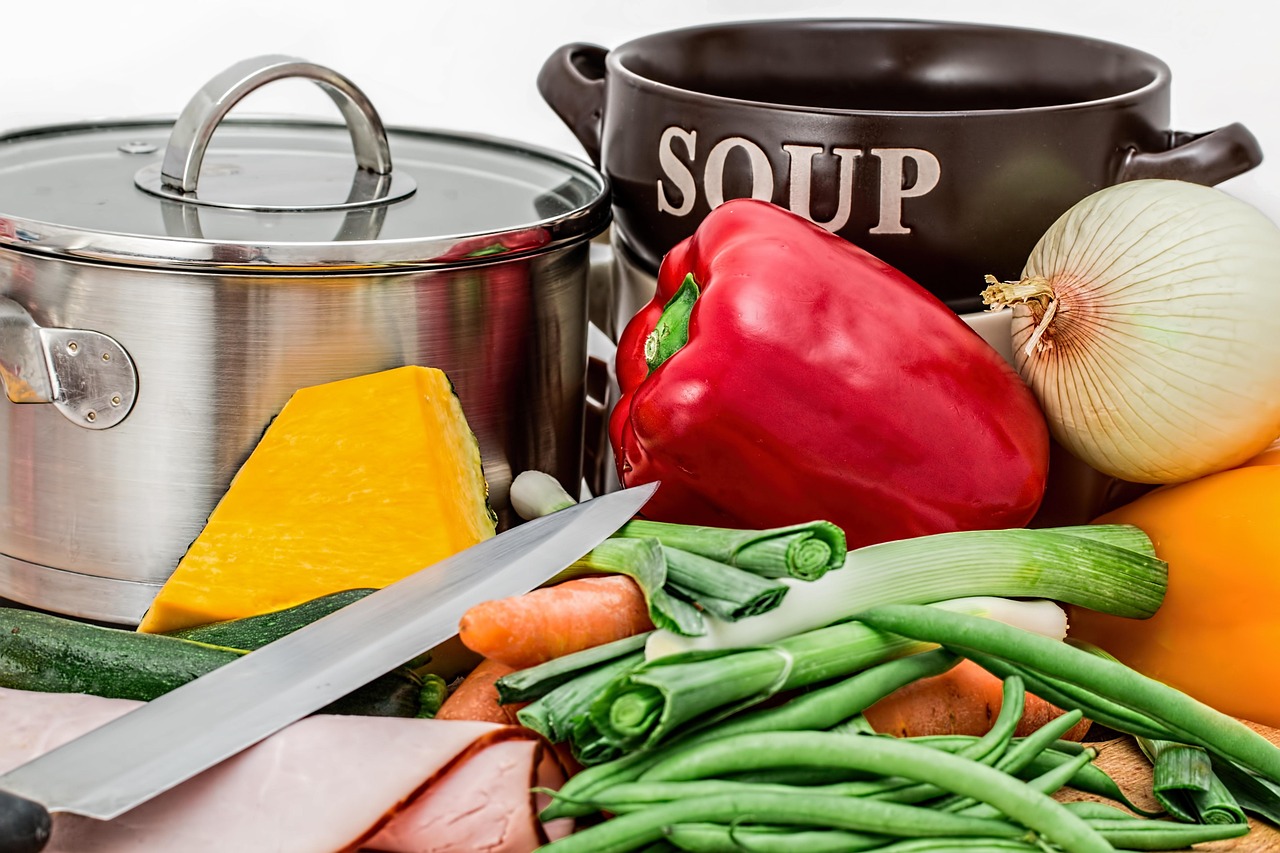 Ingredientes frescos como vegetais coloridos e legumes ao lado de panelas para o preparo de uma refeição saudável.